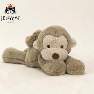 May include: A plush monkey toy with soft, textured light brown fur, a cream-colored face, and a dark brown nose. The stuffed animal is in a lying position with its head resting on its front paws. The Jellycat London logo is visible in the corner.