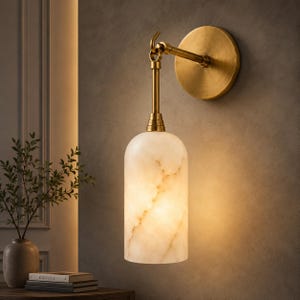 Könnte beinhalten: Eine Wandleuchte mit einem zylindrischen, weiß marmorierten Glasschirm, der an einem messingfarbenen Metallarm hängt. Die Leuchte verfügt über eine runde Wandplatte aus Messing und eine hakenförmige Halterung für die Lampe.
