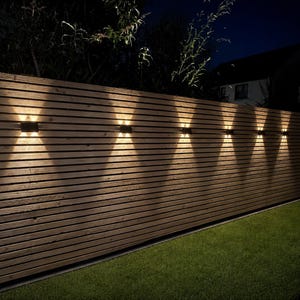 May include: A horizontal wooden slat fence featuring six rectangular wall-mounted light fixtures. Each fixture emits a bright, warm white light in an upward and downward X-shaped pattern against the natural brown wood grain of the fence panels.