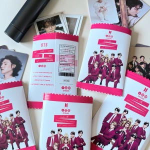 Könnte beinhalten: Eine Sammlung von BTS Arirang Snack-Tüten mit rosa-weißer Verpackung und Gruppenfotos der Mitglieder in roten Anzügen und Kronen. Die Tüten enthalten Nährwertangaben, Textbeschriftungen und einzelne Fotokarten der Mitglieder.