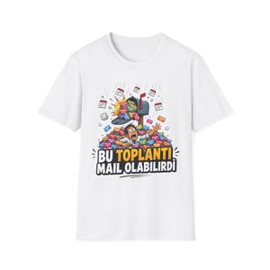 以下が含まれることがあります： 白い半袖Tシャツ。郵便受けから溢れ出る色とりどりの会議招待カードの山に埋もれた人物のグラフィックイラストが描かれています。グラフィックの下には「BU TOPLANTI MAIL OLABILIRDI」という太字のテキストがプリントされています。