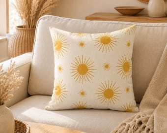 May include: A square throw pillow featuring a repeating pattern of mustard yellow suns with radiating rays on an off-white background. The suns vary in size, creating a scattered arrangement across the fabric surface of the decorative cushion.
