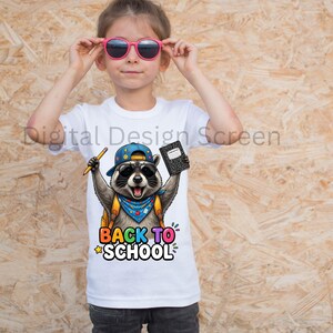 Puede incluir: Una camiseta blanca con un gráfico de un mapache que lleva una gorra azul, gafas de sol y un pañuelo azul. El mapache sostiene un lápiz amarillo y un cuaderno negro. Debajo del gráfico, el texto BACK TO SCHOOL aparece en letras coloridas.