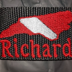 May include: A rectangular black embroidered patch featuring a red and white graphic of the state of North Carolina. Below the state shape, the name Richard is stitched in bold red thread. The patch has a textured, woven fabric appearance.