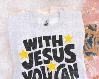May include: A light gray crewneck sweatshirt featuring the black distressed text "WITH JESUS YOU CAN" arranged in three lines, accented by four bright yellow stars positioned around the lettering. The garment has a standard ribbed collar.