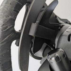 May include: A black racing steering wheel attachment featuring extended paddle shifters. The steering wheel rim is wrapped in black tape, and the paddle shifters are mounted with a 3D-printed bracket, showing a matte finish and textured surface.