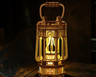 Può includere: Una lanterna in legno chiaro con intricati motivi geometrici e ad arco tagliati al laser. La struttura include una maniglia superiore e un nucleo centrale illuminato che emette una calda luce gialla, mettendo in risalto i dettagli.