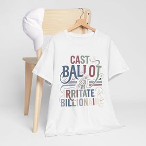May include: A white short-sleeved t-shirt and a matching white baseball cap. The t-shirt features a graphic design with the text "CAST A BALLOT IRRITATE A BILLIONAIRE" in multi-coloured lettering, accompanied by an illustration of a hand holding a ballot.