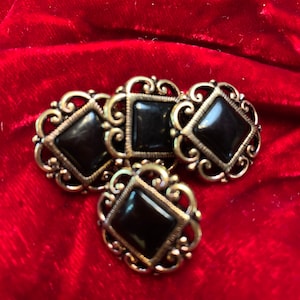 May include: Four black and gold decorative buttons with ornate designs. Each button has a square black stone in the center.