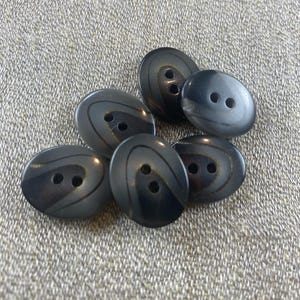 May include: A collection of seven dark gray oval buttons with two holes each. The buttons have a subtle, swirled design in a slightly lighter shade of gray, adding a touch of elegance. These buttons are ideal for sewing projects.
