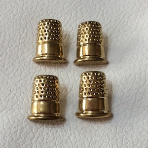 May include: Four gold-colored metal thimbles with a textured pattern. The thimbles are arranged in a square pattern on a white surface.