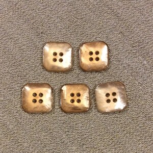 May include: Five brown plastic buttons with four holes each. The buttons are arranged in a row.
