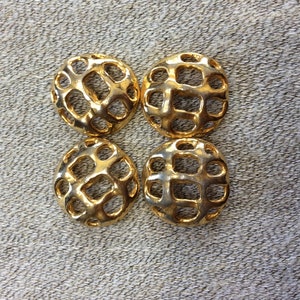May include: Four gold-colored metal buttons with a geometric, openwork design. The buttons are round and have a raised, textured surface.