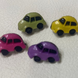 May include: Four plastic car buttons in different colors: green, yellow, pink, and purple. Each button has a black window and black wheels.