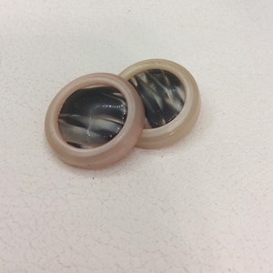 May include: Two round, cream-colored buttons with a black and white swirl design.