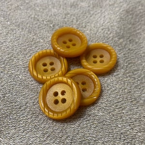 May include: Five gold-colored plastic buttons with four holes each. The buttons have a raised, textured design around the edges.