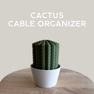 Pode incluir: Um organizador de cabos em forma de cacto verde-oliva escuro com um corpo cilíndrico canelado e topo plano. O objeto está colocado dentro de um vaso branco liso e cônico. O texto CACTUS CABLE ORGANIZER é exibido em letras brancas acima do objeto.
