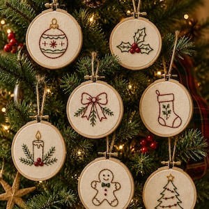 May include: A set of seven circular wooden embroidery hoops featuring hand-stitched designs on off-white fabric. The motifs include a Christmas bauble, holly leaves, a bow, a stocking, a candle, a gingerbread person, and a Christmas tree.