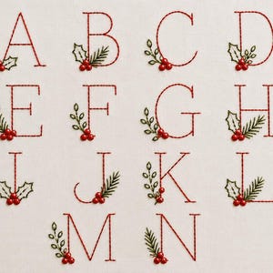 May include: A set of embroidered capital letters from A to N stitched in red thread on a white fabric background. Each letter is decorated with green holly leaves and small red berries, creating a festive botanical design for each character.