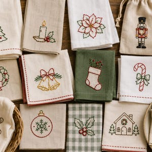 May include: A collection of folded fabric napkins and a drawstring pouch featuring embroidered Christmas motifs including a tree, candle, poinsettia, nutcracker, wreath, bells, stocking, candy cane, gingerbread man, ornament, holly, house, and rocking horse.