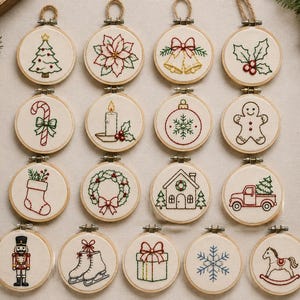 May include: A collection of sixteen circular wooden embroidery hoops featuring various Christmas-themed designs stitched in red, green, and gold thread on off-white fabric, including a tree, poinsettia, bells, holly, candy cane, candle, ornament, gingerbread man, stocking, wreath, house, truck, nutcracker, ice skates, gift, snowflake, and rocking horse.