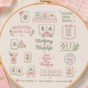 May include: A round wooden embroidery hoop containing white fabric with colorful stitched designs of Mahjong tiles, flowers, bows, and text including Mahjong Social Club, Mahjong is Mahlife, Hot Moms Play Mahjong, and Play Together Laugh Together Win Together.