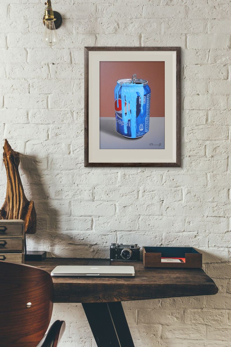 Puede incluir: Una pintura enmarcada de una lata de Pepsi azul y roja con pintura azul goteando por el lado. La lata est&aacute; sobre una superficie gris con un fondo marr&oacute;n.