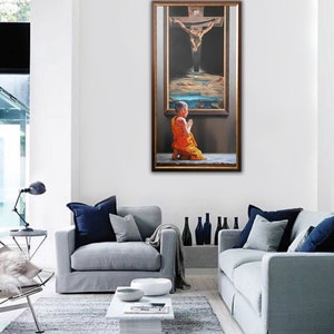 May include: A painting of a person kneeling in prayer in front of a framed image of a man on a cross. The person is wearing a yellow robe and the background is dark.