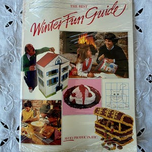 Pode incluir: Um folheto vintage da Avon Products, Inc. intitulado The Best Winter Fun Guide. A capa apresenta várias fotografias, incluindo uma pessoa a pintar uma casa de bonecas, uma família perto de uma lareira, uma sobremesa, um desenho de um gato e um baú.