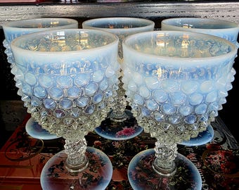 May include: A set of four opalescent white glass goblets featuring a raised hobnail texture on the bowl, a twisted stem, and a circular base. The glass displays a milky, semi-translucent quality with subtle blue and iridescent highlights.