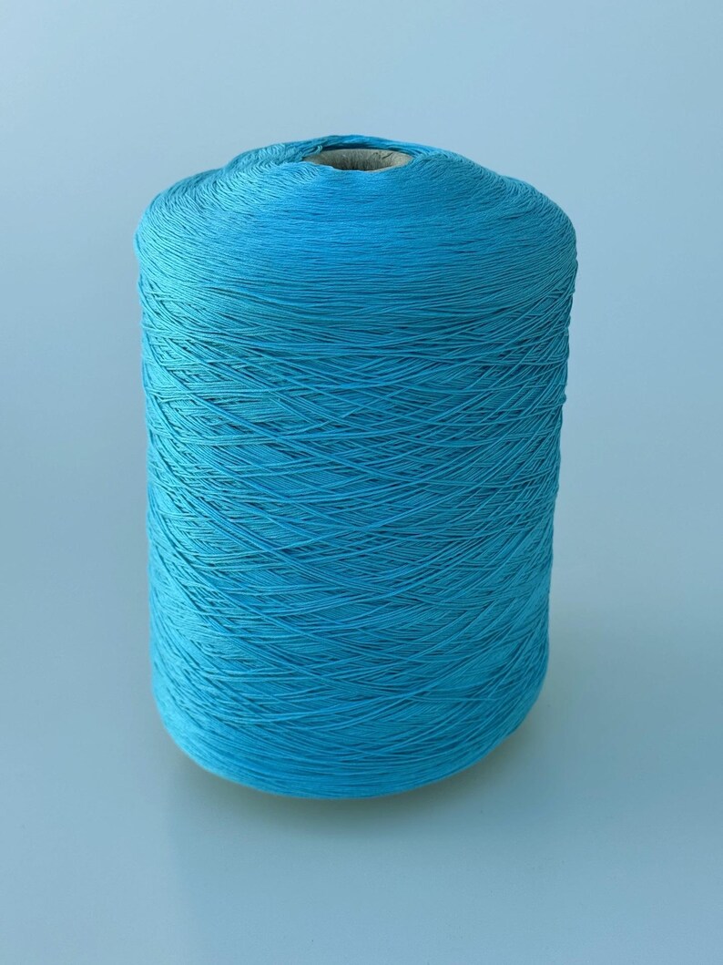 May include: A large cylindrical spool of vibrant turquoise blue yarn. The thread is tightly wound in a cross-hatch pattern around a central cardboard core, creating a textured surface with a consistent, bright color throughout the entire object.