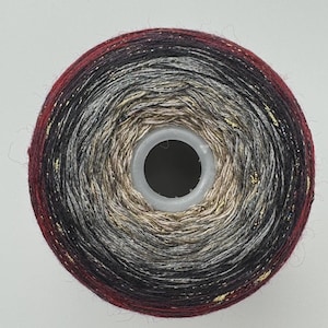 May include: A circular spool of yarn featuring a gradient color transition from a deep burgundy outer edge to a black middle, transitioning into a light grey and finally a beige center, all interwoven with thin, shimmering gold metallic threads.