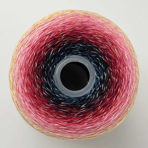 May include: A circular yarn cake featuring a gradient color transition from a dark navy blue center to vibrant shades of magenta and pink, finishing with a soft yellow outer edge. The yarn has a subtle metallic shimmer throughout the fibers.