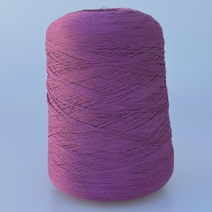 May include: A large, cylindrical spool of deep purple yarn. The thread is tightly wound in a crisscross pattern around the central core, creating a textured surface. The spool stands upright, displaying a consistent, rich violet hue throughout.