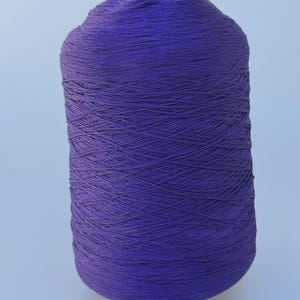 May include: A cylindrical spool of deep purple yarn wound tightly in a cross-hatch pattern. The thread is thin and uniform, creating a smooth, dense texture across the entire surface of the spool, which stands upright against a plain background.
