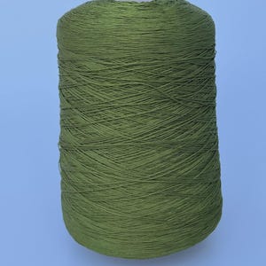May include: A large, cylindrical spool of olive green yarn. The thread is tightly wound in a crisscross pattern around the central core, creating a uniform, textured surface across the entire exterior of the spool from top to bottom.