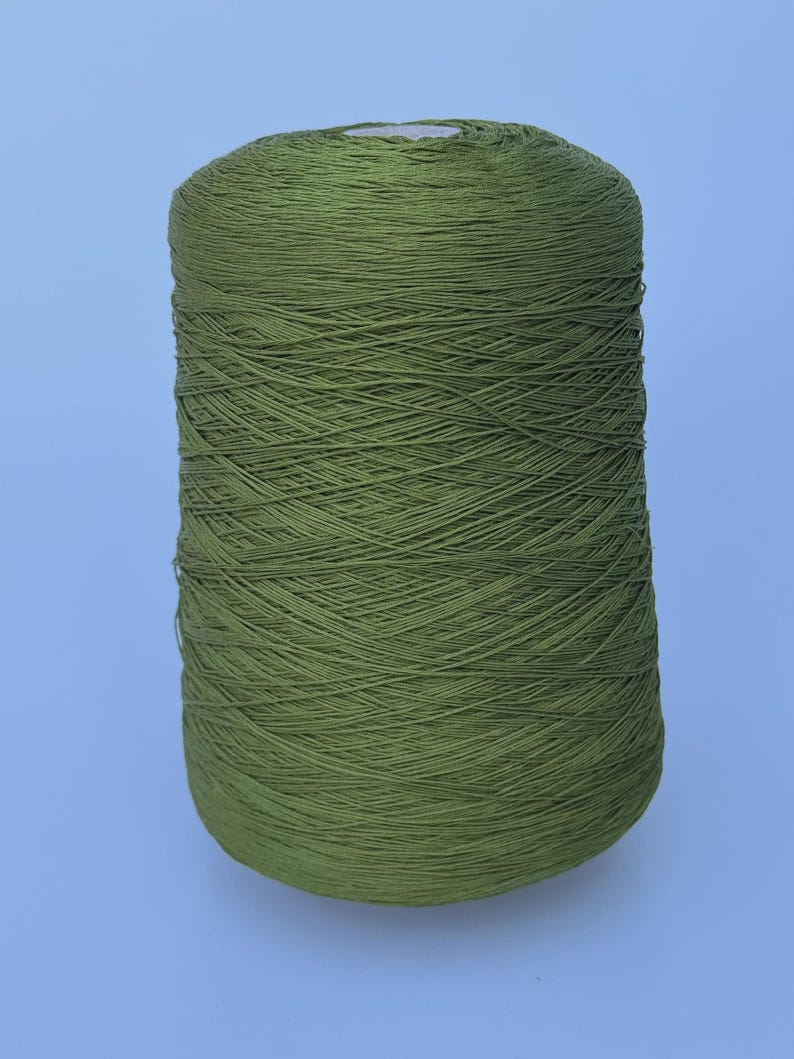 May include: A large, cylindrical spool of olive green yarn. The thread is tightly wound in a crisscross pattern around the central core, creating a uniform, textured surface across the entire exterior of the spool from top to bottom.