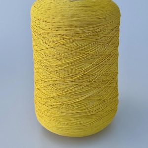 May include: A large cylindrical spool of vibrant yellow yarn. The thread is wound tightly in a crisscross pattern around a central core, creating a textured surface with visible individual strands of fiber throughout the entire spool.