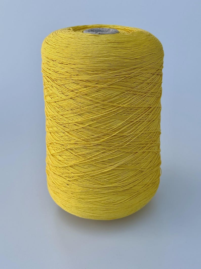 May include: A large cylindrical spool of vibrant yellow yarn. The thread is wound tightly in a crisscross pattern around a central core, creating a textured surface with visible individual strands of fiber throughout the entire spool.