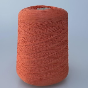 May include: A large, cylindrical spool of vibrant terracotta-colored yarn. The thread is tightly wound in a cross-hatch pattern around a central core, creating a uniform, textured surface that tapers slightly toward the top of the spool.