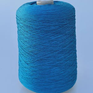 May include: A large cylindrical spool of vibrant turquoise blue yarn. The thread is tightly wound in a crisscross pattern around the central core, which is visible at the top. The spool has a smooth, uniform shape and a consistent bright blue color.