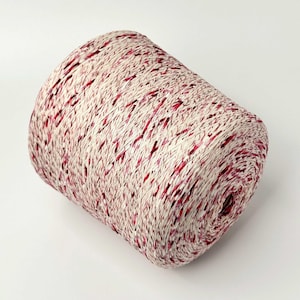May include: A cylindrical spool of yarn featuring a blend of off-white and deep red fibers. The yarn is tightly wound, creating a textured appearance with a consistent distribution of the red color throughout the light-colored base material.
