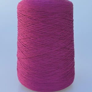 May include: A large cylindrical spool of vibrant magenta yarn. The thread is tightly wound in a crisscross pattern around the central core, creating a textured surface with a consistent deep pink color throughout the entire spool.