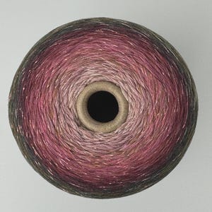 May include: A circular spool of yarn featuring a gradient color transition from a dark charcoal gray on the outer edges to a vibrant magenta and soft pink in the center, with subtle metallic threads woven throughout the fiber texture.