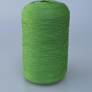 May include: A cylindrical spool of vibrant lime green yarn, tightly wound with a smooth, consistent texture. The thread is wrapped in a uniform pattern around the central core, creating a solid, dense appearance for this craft supply.