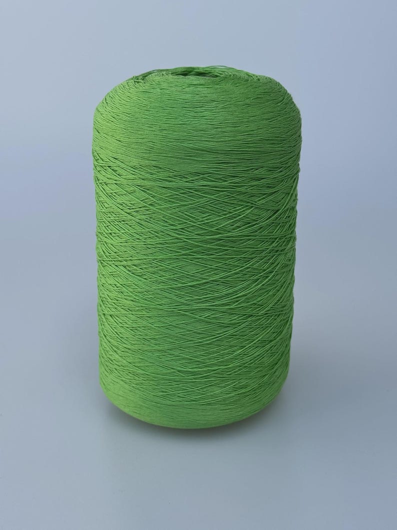 May include: A cylindrical spool of vibrant lime green yarn, tightly wound with a smooth, consistent texture. The thread is wrapped in a uniform pattern around the central core, creating a solid, dense appearance for this craft supply.
