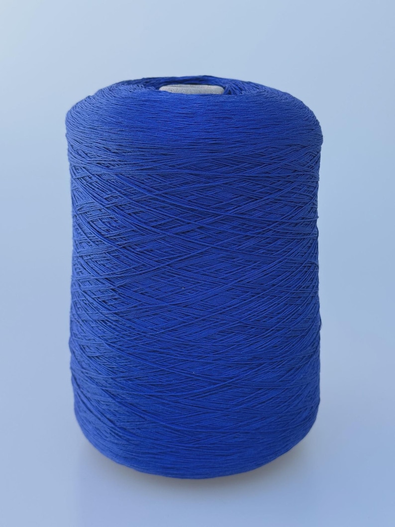 May include: A large cylindrical spool of vibrant royal blue yarn. The thread is tightly wound in a crisscross pattern around the central core, creating a uniform and dense texture throughout the entire surface of the spool.