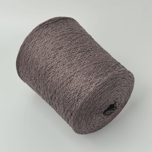 May include: A large cylindrical spool of dark brown yarn with a textured, multi-tonal appearance. The thread is tightly wound around a central core, creating a dense, uniform surface with visible fiber strands throughout the entire spool.