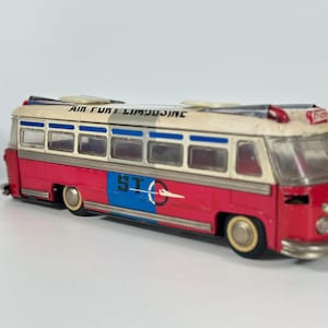 May include: A vintage toy bus with a red and white body, featuring blue accents and the text AIR PORT LIMOUSINE and STO on the side. The bus has silver-colored trim, clear windows, and small wheels, with a small red light on the roof and a front emblem.