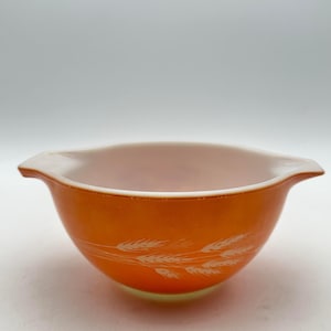 May include: A bright orange glass bowl with two side handles and a white wheat stalk pattern encircling the exterior. The bowl features a smooth, glossy finish and a wide, open top, showcasing a classic design with a vibrant, solid colour.